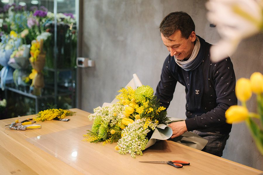 Business Insurance - A Happy Florist is Preparing a Bouquet of Yellow Flowers for a Client on a Table at His Flower Shop